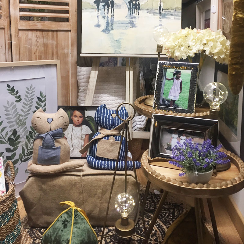 Foto de un mueble con varios marcos de fotos, peluches de gatos y plantas con flores de plástico