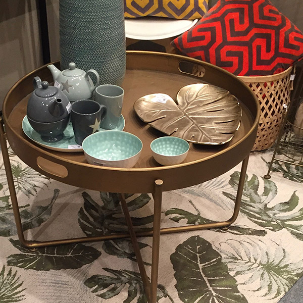 Foto de una mesa con una bandeja en forma de hoja dorada y unas tazas a juego con unas teteras grises, hay dos modelos, uno mas claro y uno mas oscuro.